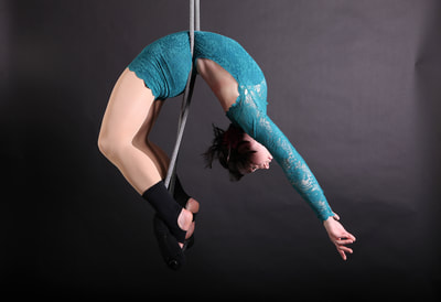 Photo of a white woman in a teal leotard doing a backbend on a trapeze.